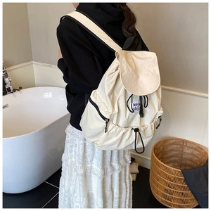 Detail of cream nylon backpack with black drawstring closure and stylish flap design
