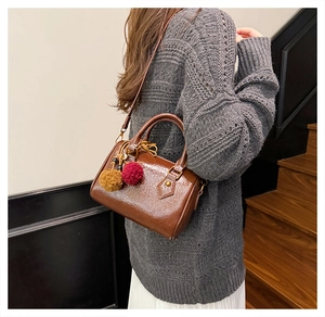 Close-up of a brown glossy barrel bag with pompom charm and golden metal hardware