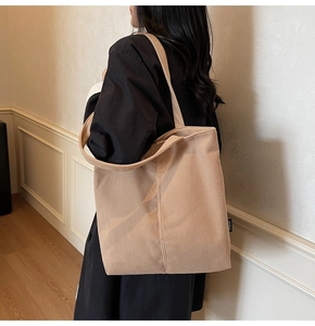 Detail of beige corduroy tote bag showing wide ribbed fabric texture and side brand label