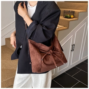 Brown suede crossbody bag with large decorative bow detail shown on fashion model