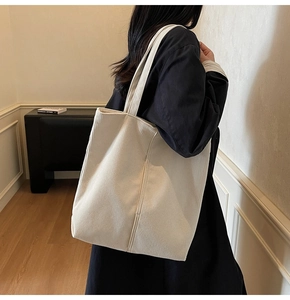 Close-up of a large beige corduroy tote bag worn over the shoulder by a model