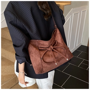 Detail of a brown suede tote bag featuring a decorative bow and metallic accents