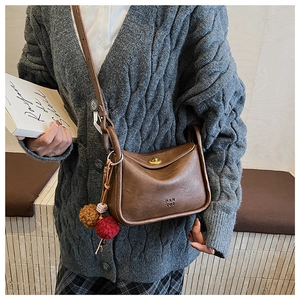 Close-up of brown PU leather pillow bag with gold twist lock and plush pom-pom charm
