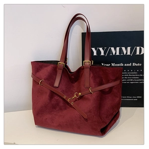 Detail of burgundy suede tote bag with leather straps and decorative metallic buckles