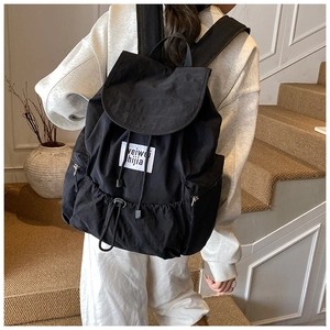 Detail of a large black nylon backpack with flap drawstring and woven label shown on model
