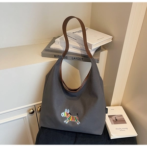 Detail of grey canvas tote bag featuring rainbow zebra embroidery and brown leather straps