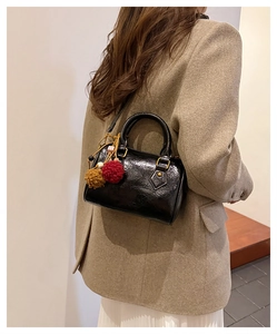 Close-up of black glossy barrel bag with plush pendant on a model for daily styling