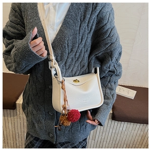 Detail of cream pillow bag featuring gold twist lock and brown plush pompom charm