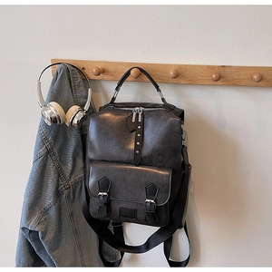 Detail of dark gray retro backpack with metallic buckles hanging against a clean wall