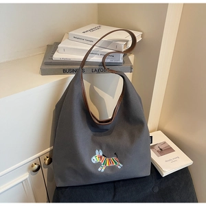 Detail of grey canvas tote bag featuring colorful zebra embroidery and brown leather straps