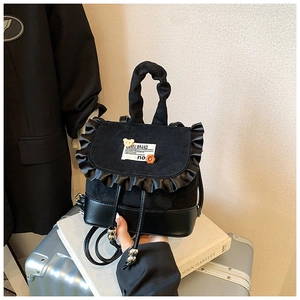 Detail of black mini dual-use backpack featuring satin ruffle trim and bear patch