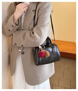 Detail of black glossy wrinkled texture barrel bag with a two-tone fur pompom charm
