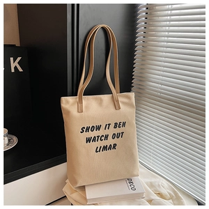 Détail d'un sac cabas en toile beige avec imprimé noir posé sur un livre décoratif