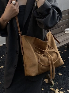 Brown frosted suede tote bag with drawstring bow detail on a classic outdoor bench