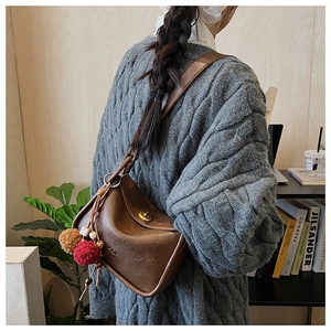Detailed view of brown leather pillow bag with stylish charm on a textured grey sweater