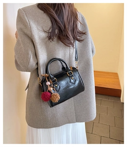 Detail of a black mini Boston bag with brown pompom charm worn over a gray blazer