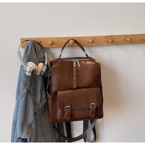 Detail of vintage brown PU leather backpack hanging on a rack with fashion accessories