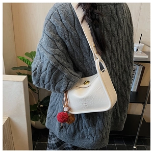 Detail of cream leather shoulder bag featuring a gold twist lock and plush charm accessory