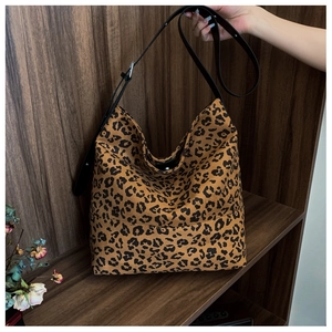 Detail of leopard print tote bag with black leather strap on a rustic wooden shelf