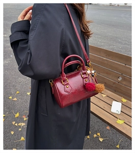 Detail of burgundy cylinder bag with plush charm and bead decor in autumn outdoor setting