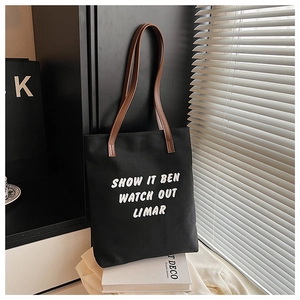 Détail d'un grand sac cabas en toile noire avec typographie blanche et anses en cuir marron