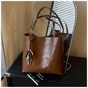 Macro shot of large brown leather tote bag with wooden bead pendant and polished surface
