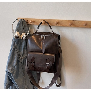 Detail of vintage brown leather backpack hanging with denim jacket and headphones