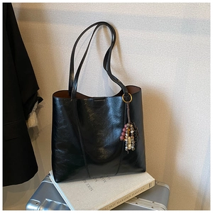 Close-up of black glossy leather tote bag with vintage bead charm on travel suitcase