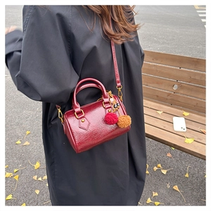 Close-up of wine red embossed cylinder bag with pompom charms and autumn outdoor details