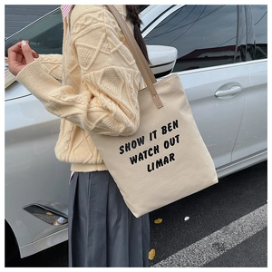 Détail d'un sac fourre-tout en toile crème avec lettrage noir et fines lanières en cuir