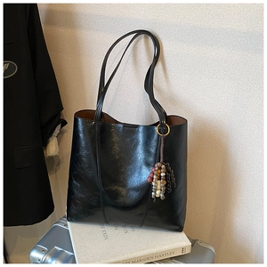 Detail of black faux leather tote bag with colorful bead charm on a silver suitcase