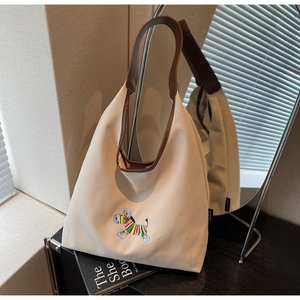 Detail of beige canvas tote bag with rainbow zebra embroidery and leather handles