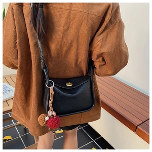 Detail of black leather crossbody bag with vintage gold clasp and plush ball charm decor