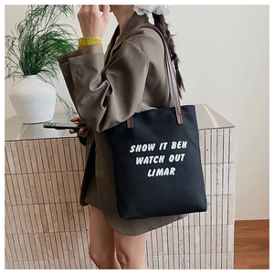 Détail d'un sac fourre-tout en toile noire avec lanières brunes et texte blanc imprimé