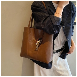 Detail of a brown vintage tote bag featuring a colorful beaded tassel charm and leather texture