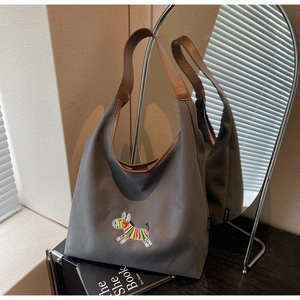 Close-up of zebra embroidery on dark grey canvas tote bag with brown leather handles