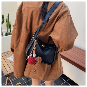 Detail of black leather shoulder bag with plush charm on brown corduroy jacket