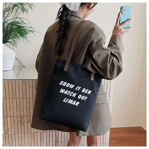 Détail du sac cabas en toile noire avec anses marron et impression de lettres blanches