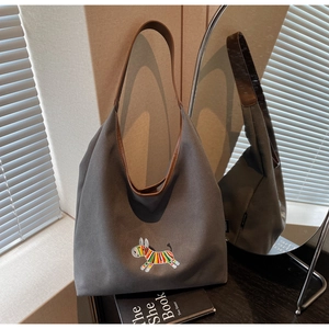 Close-up of gray canvas tote bag featuring colorful zebra embroidery and brown leather strap