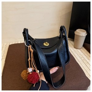 Detail of black leather bag featuring gold twist-lock and decorative pompom charm