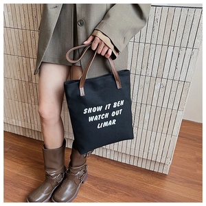 Gros plan d'un sac cabas en toile noire avec poignées en cuir marron et texte blanc