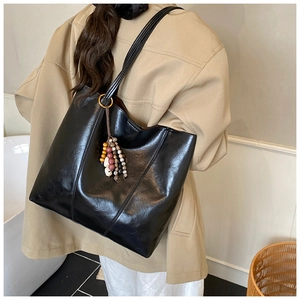 Detail of black glossy tote bag with vintage colorful wooden bead charm on shoulder