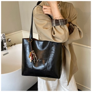 Detail of black tote bag featuring colorful wooden bead tassels on a long shoulder strap