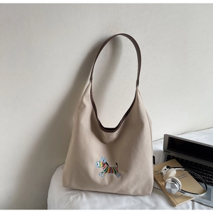 Close-up of beige canvas tote with embroidered pattern and brown leather handle strap
