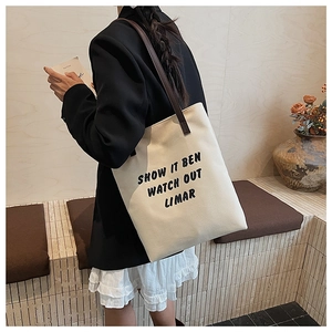 Détail d'un sac cabas en toile minimaliste avec texte noir et anses en cuir marron