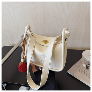 Detail of off-white tote bag featuring golden round twist lock and red plush charm accessory