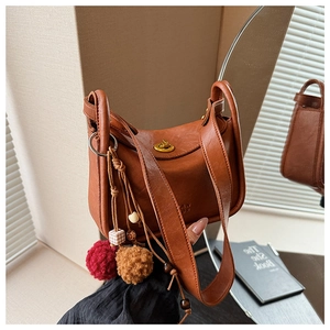 Macro detail of brown leather shoulder bag featuring vintage gold lock and bead charm