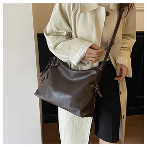 Detail of soft dark brown leather hobo bag worn by model with minimalist knot strap design