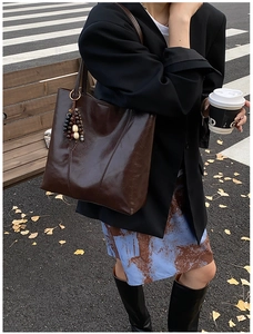 Deep brown glossy leather tote bag with retro tassel charm in an autumn street setting