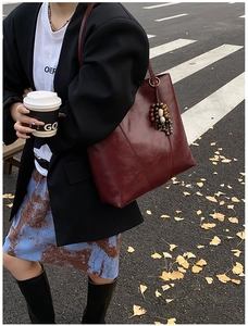 Street style view of a large burgundy leather tote bag with a vintage bead charm